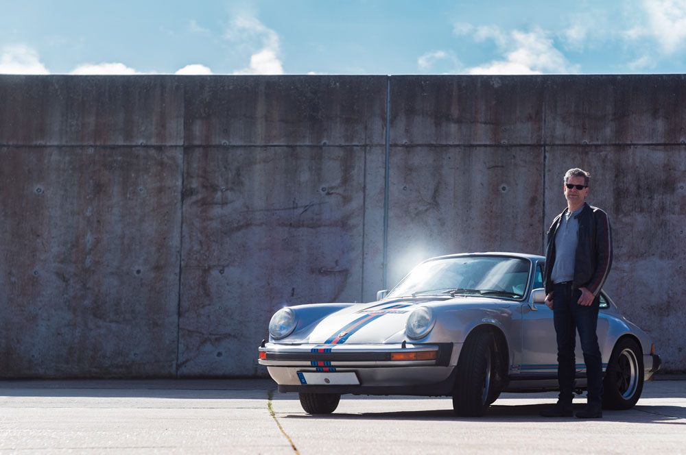 Man in leather jacket infront of his oldtimer porsche in an industrial setting