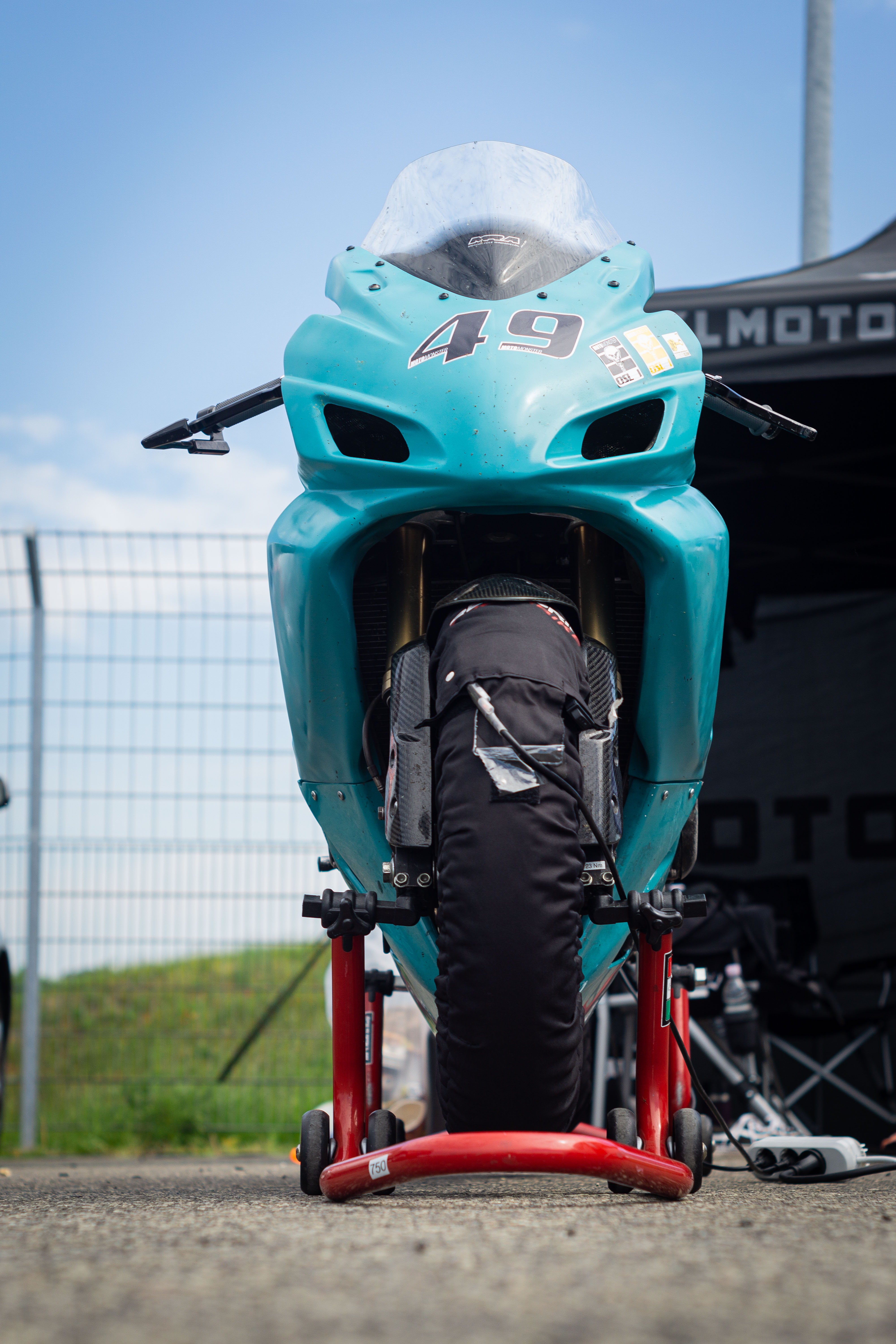 a shiny cyan colored racing motorbike on red motorbike stands with tire warmers on