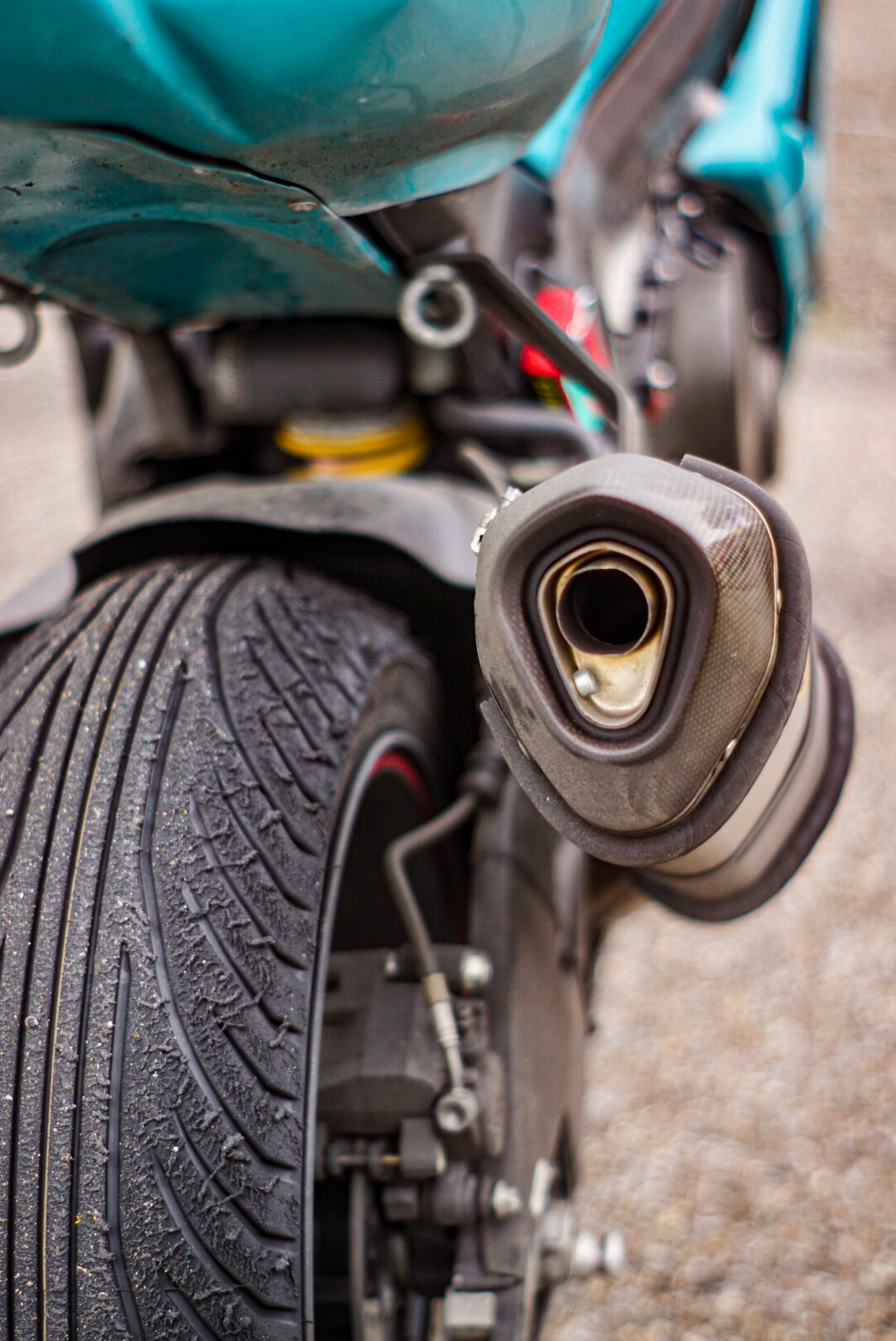 From behind photopraphed rear tyre and exhaust of turquise motorbike suzuki gsxr 750. The rear is a rain tyre that suffered a lot, one can see the rubber falling off.