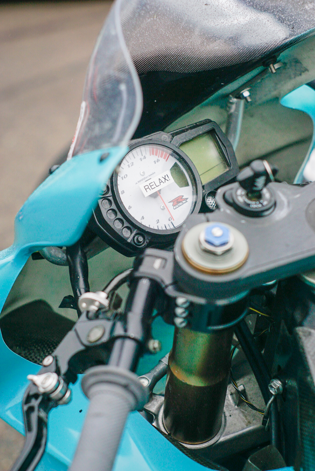 From above photopraphed view of a turquise motorbike suzuki gsxr 750 dashboard with a sticker in the middle saying 'relax'