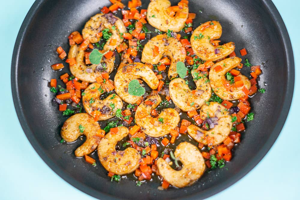 dropshot of a pan with sizzling shrymps in oil and small cut tomato plus lots of herbs