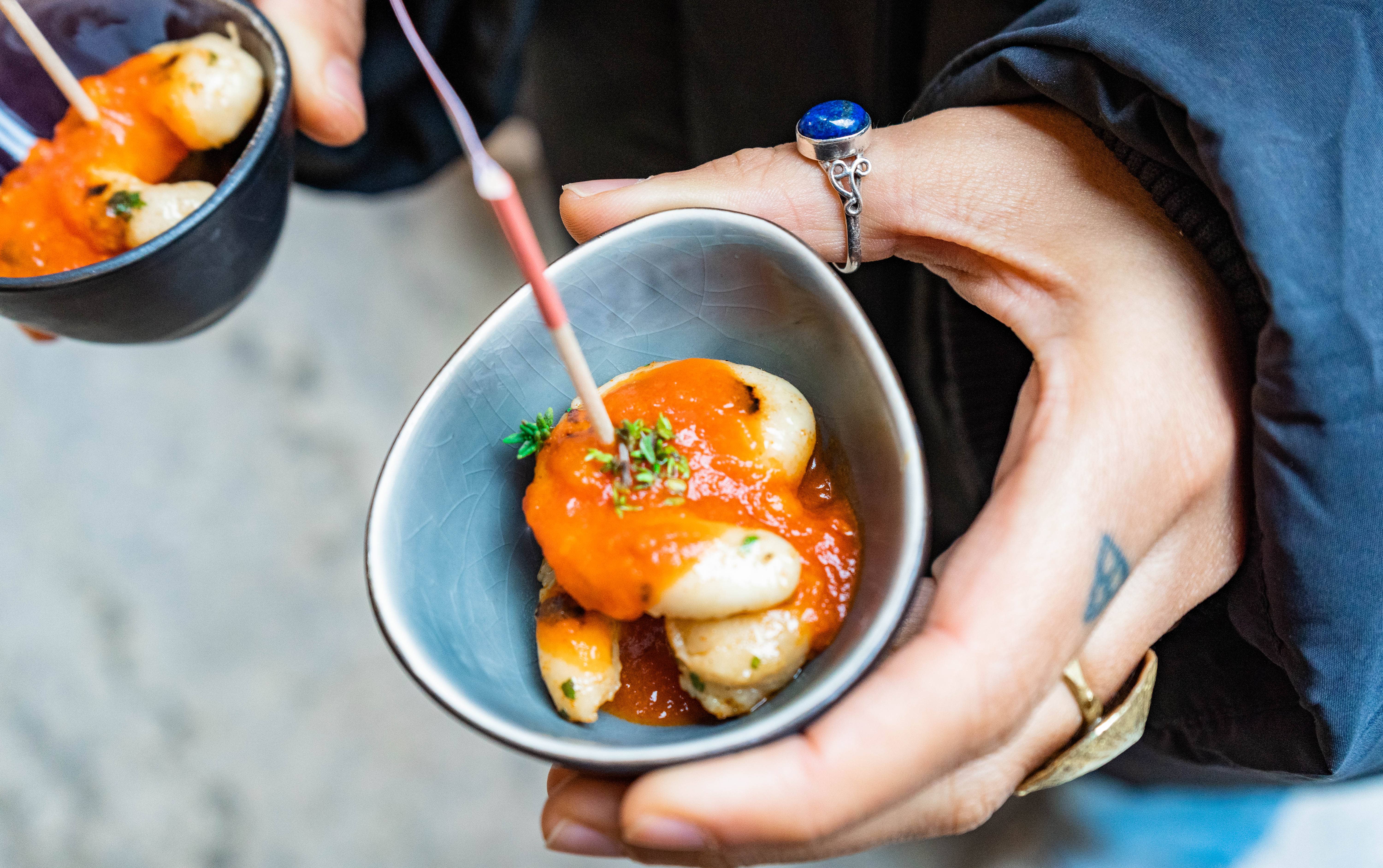 Small bowls with shrymps in tomato sauce held by a hand with tattoes and rings 